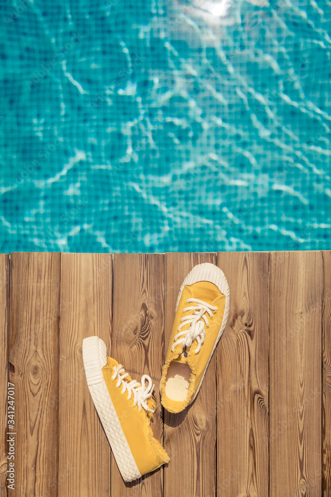 Yellow sneakers on wooden background near swimming pool