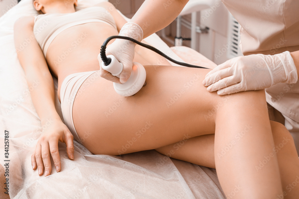 Beautiful woman undergoing procedure of anti-cellulite massage in beauty salon