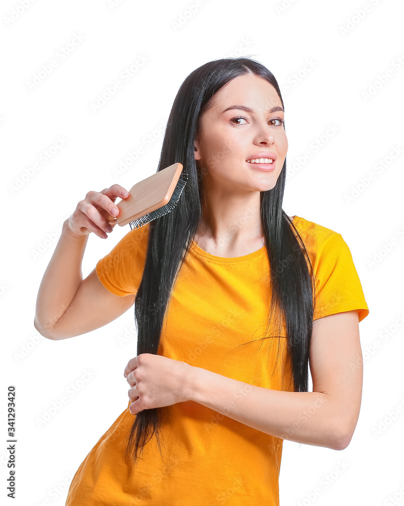 Beautiful young woman brushing hair against white background