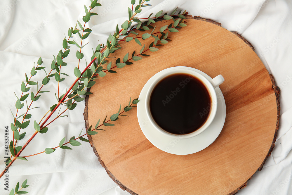 Cup of coffee and green branches on light background