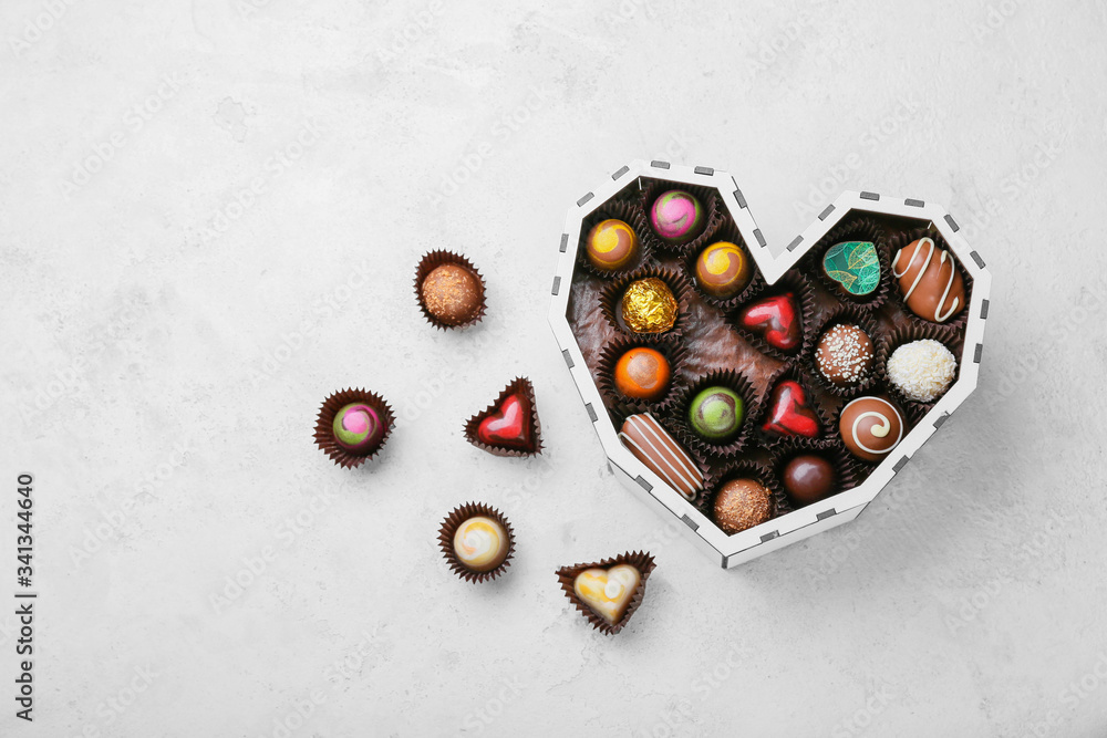 Heart-shaped box with delicious candies on light background