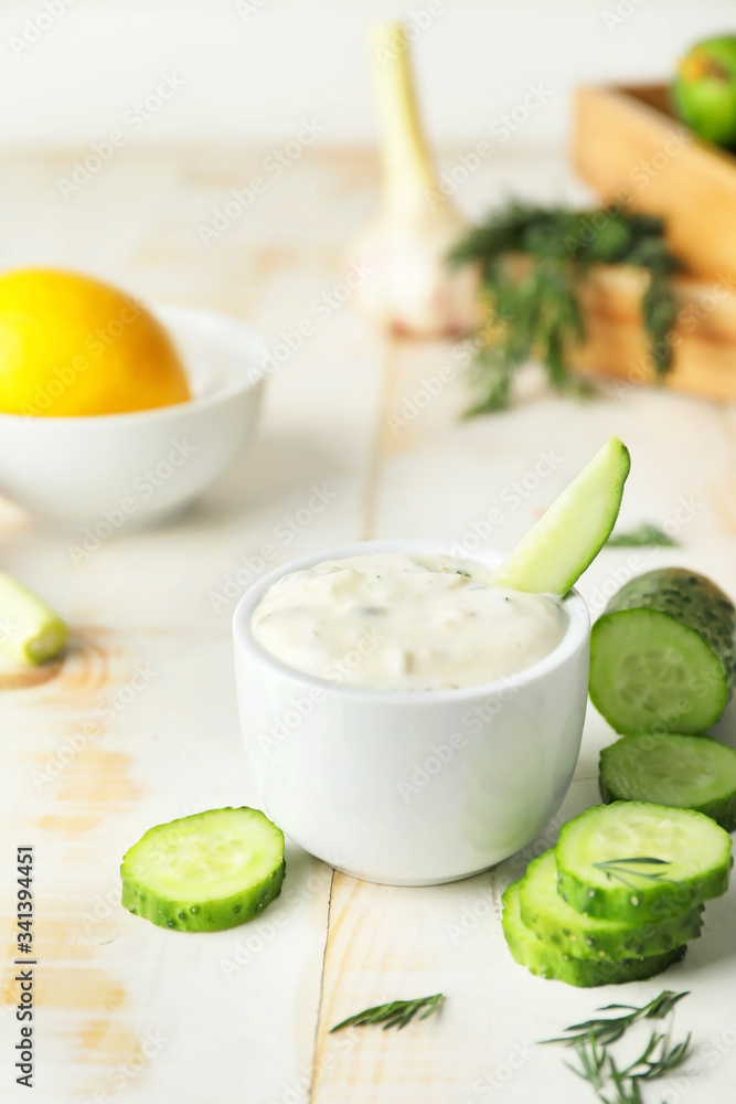 Delicious yogurt sauce with cucumber in bowl on white table