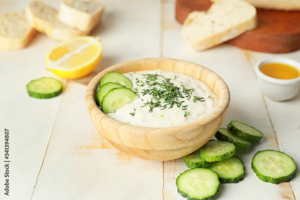 Delicious yogurt sauce with cucumber in bowl on white table