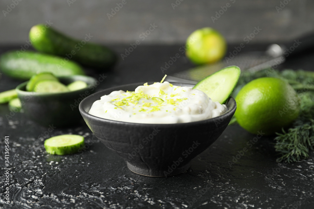 Delicious yogurt sauce with cucumber in bowl on dark background