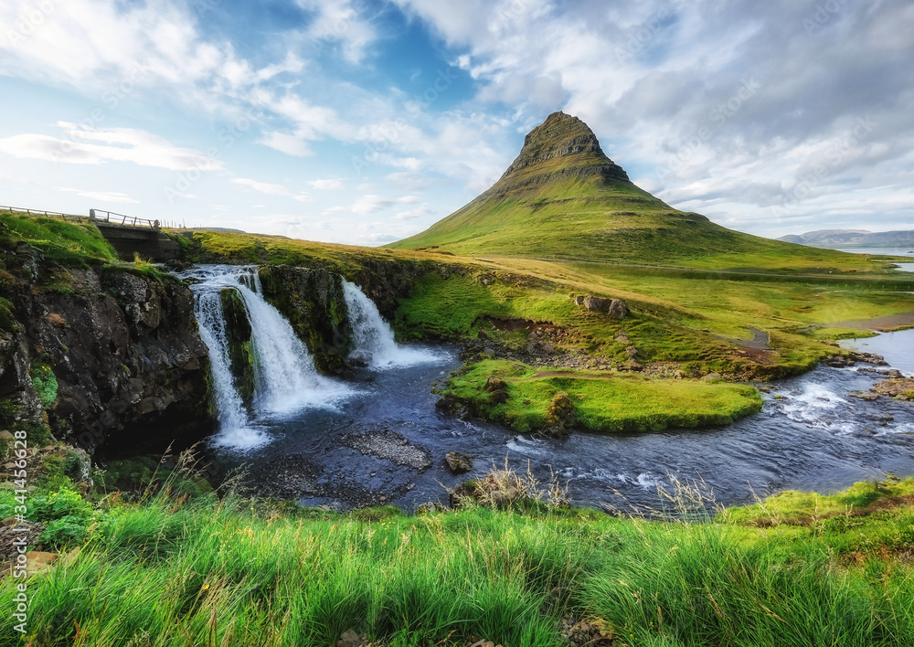 Kirkjufell mountain and waterfall in the Iceland. Natural landscape in the summer. Grass and river. 