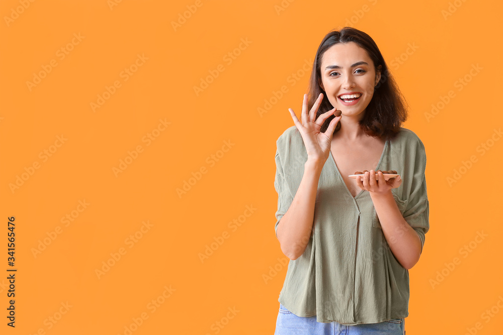 Beautiful young woman eating tasty chocolate candies on color background