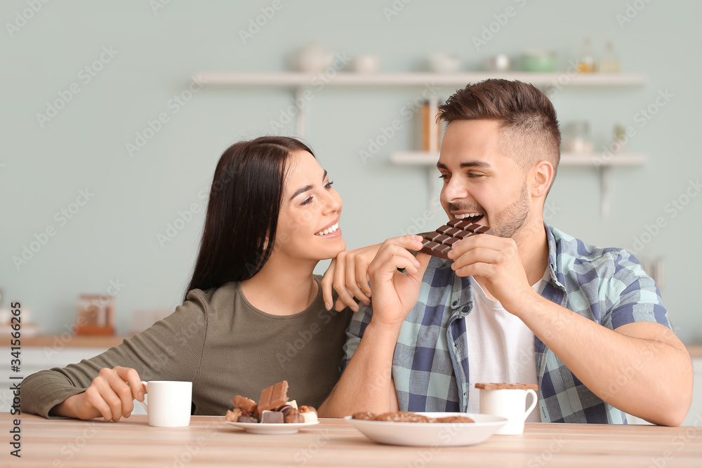 Beautiful young couple eating chocolate in kitchen