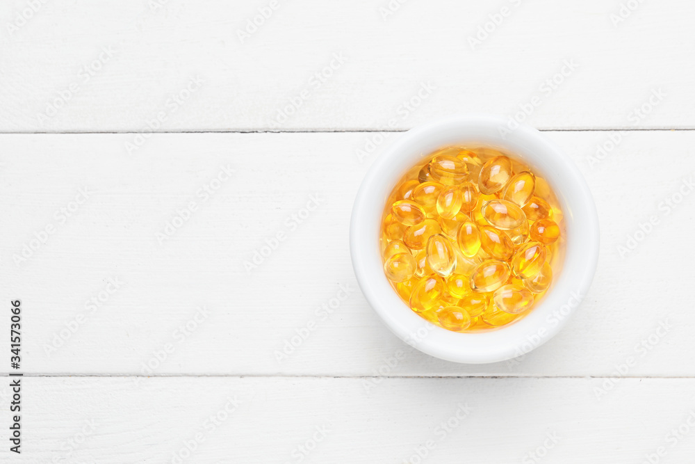 Bowl of fish oil capsules on white wooden background