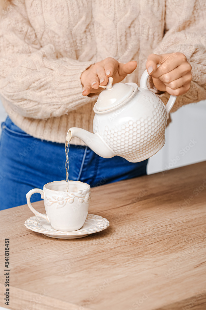 Beautiful young woman pouring tea in cup on table