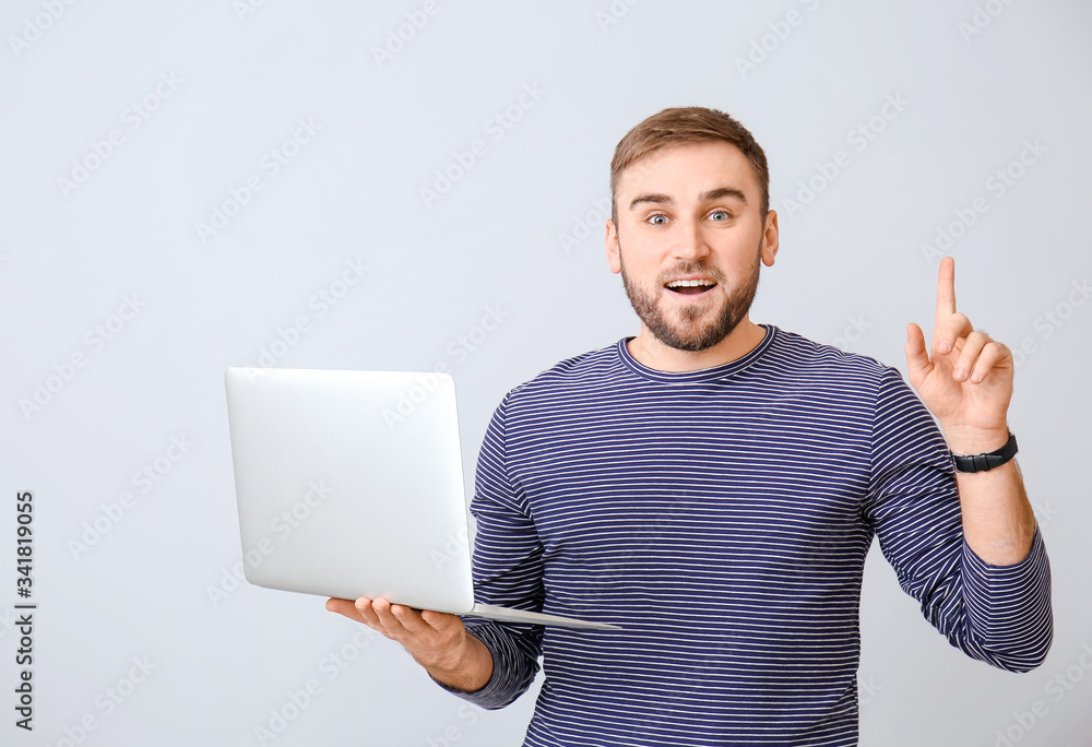 Male programmer with laptop and raised index finger on light background