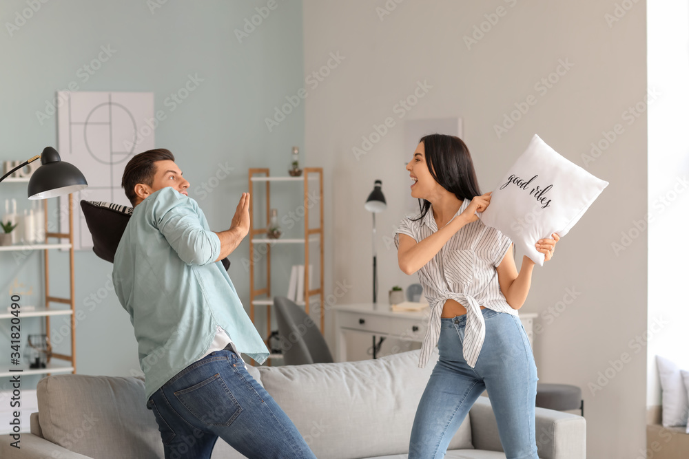 Happy young couple fighting on pillows at home