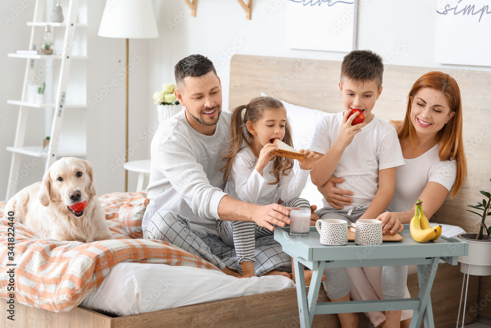 Happy family having breakfast in bedroom at home