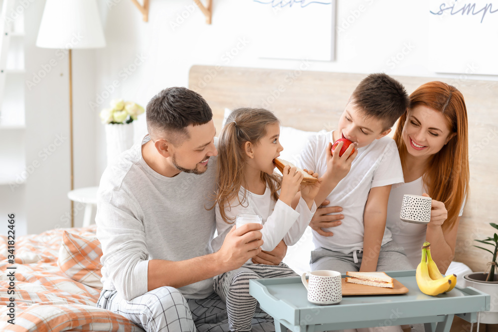 Happy family having breakfast in bedroom at home