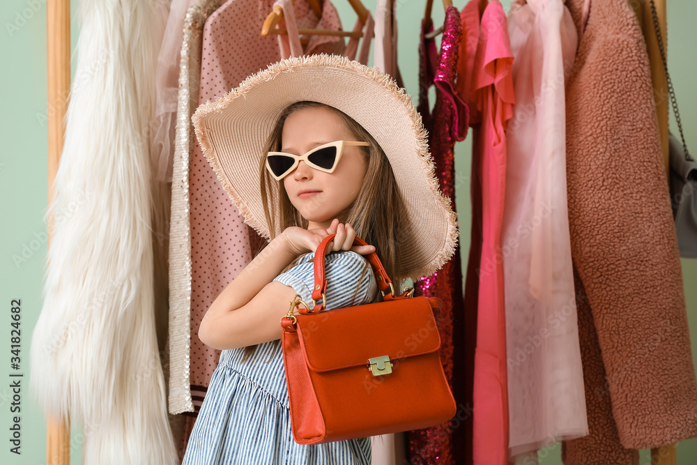 Cute fashionable girl near rack with stylish clothes on color background