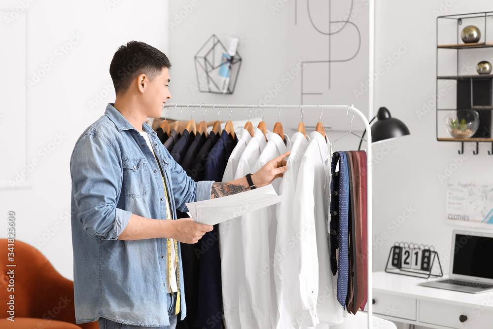 Male Asian stylist near rack with clothes in studio