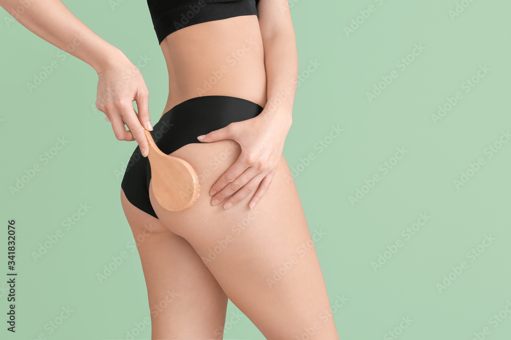 Woman with anti-cellulite massage brush on color background