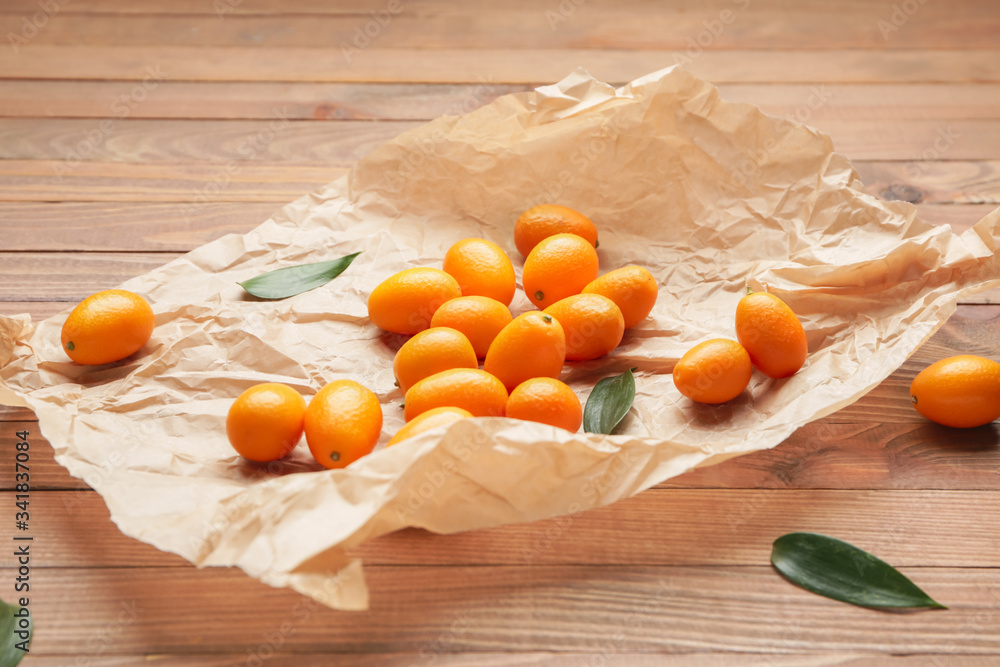 Parchment with tasty kumquat fruit on wooden background