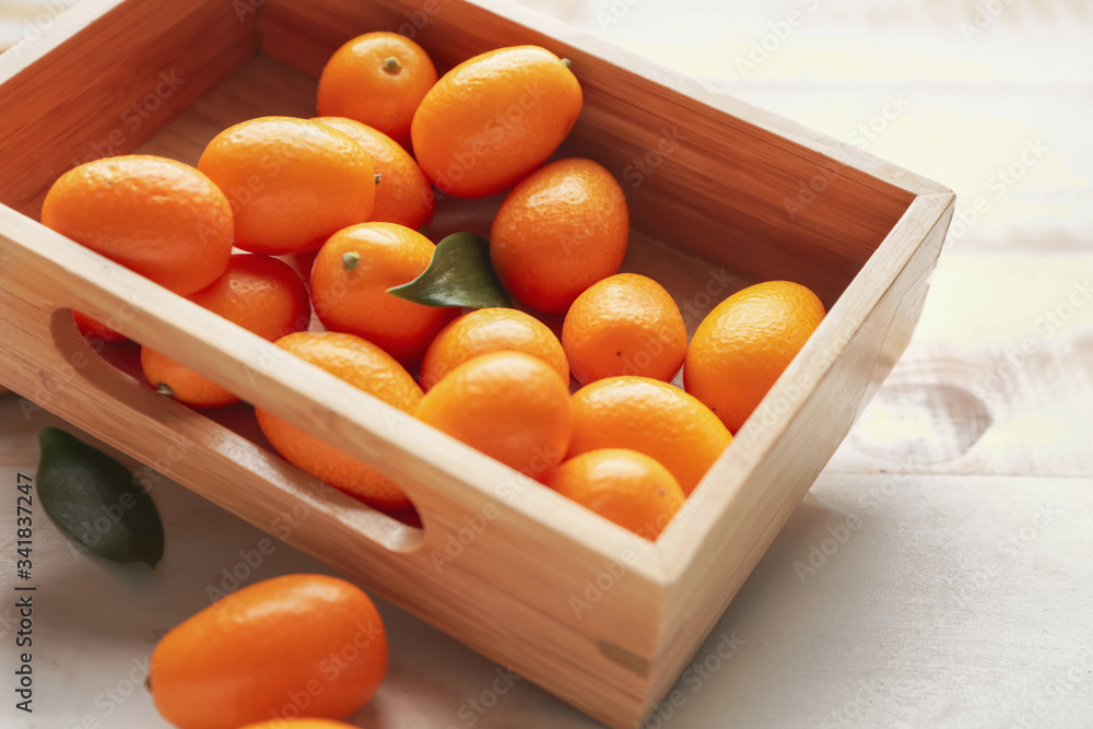 Box with tasty kumquat fruit on white wooden background