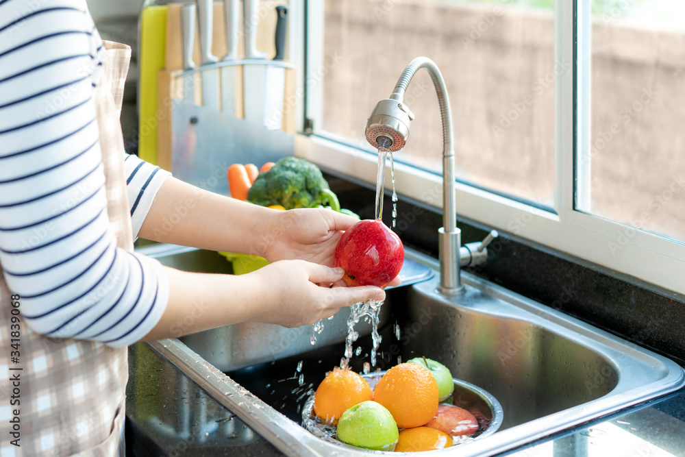 Asian healthy woman washing an apple and other fruit above kitchen sink and cleaning a fruit / veget