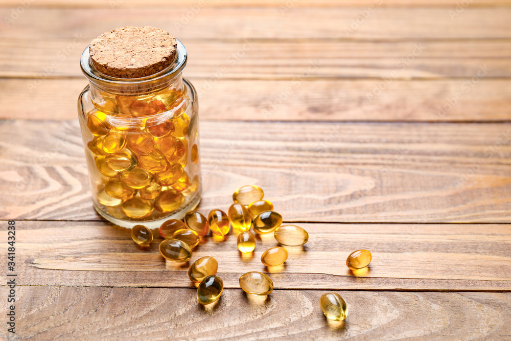 Jar with fish oil capsules on wooden background