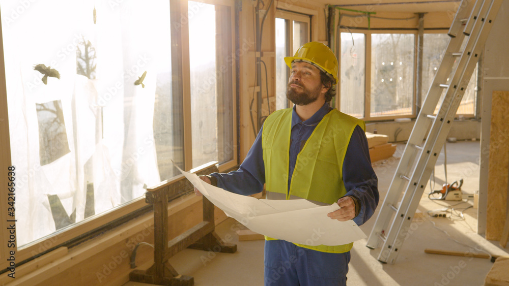 LENS FLARE: Contractor holding the construction plans looks at unfinished house.