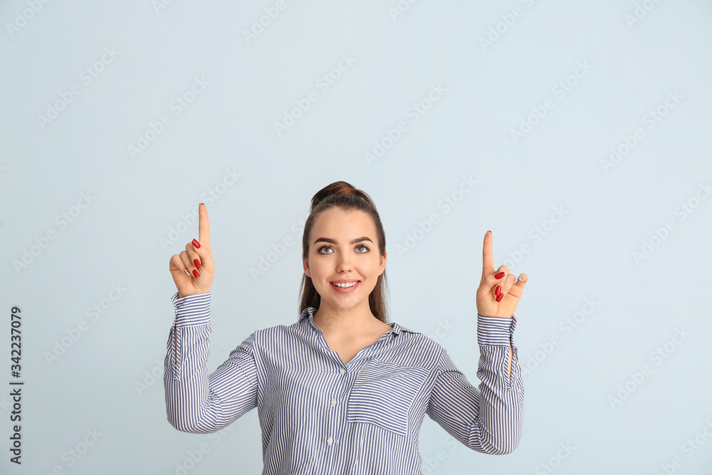 Portrait of beautiful young woman showing something on color background