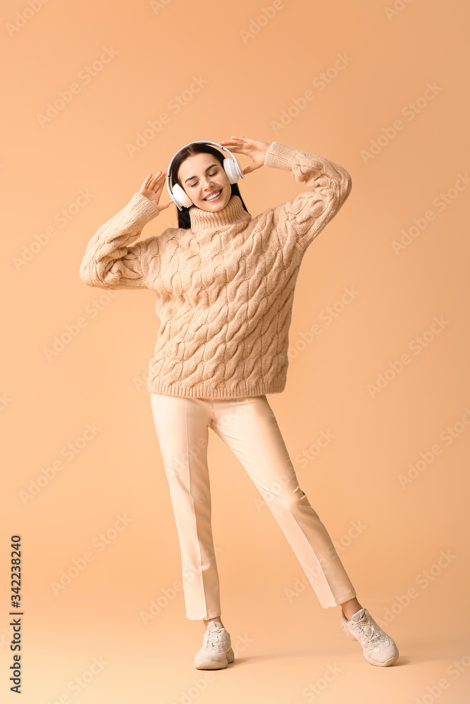 Beautiful young woman listening to music and dancing against color background