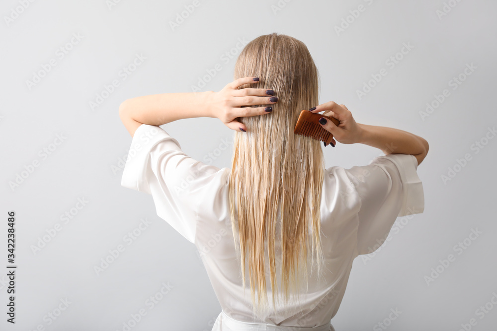 Young woman combing her hair against grey background