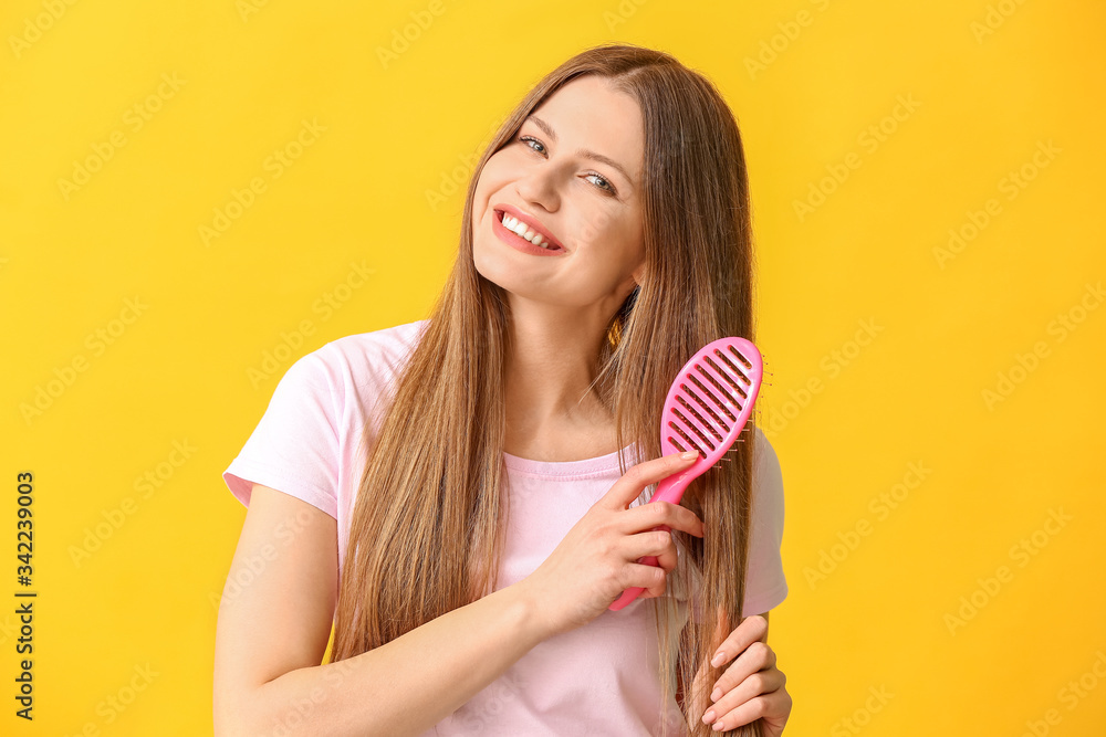 Beautiful young woman brushing hair on color background