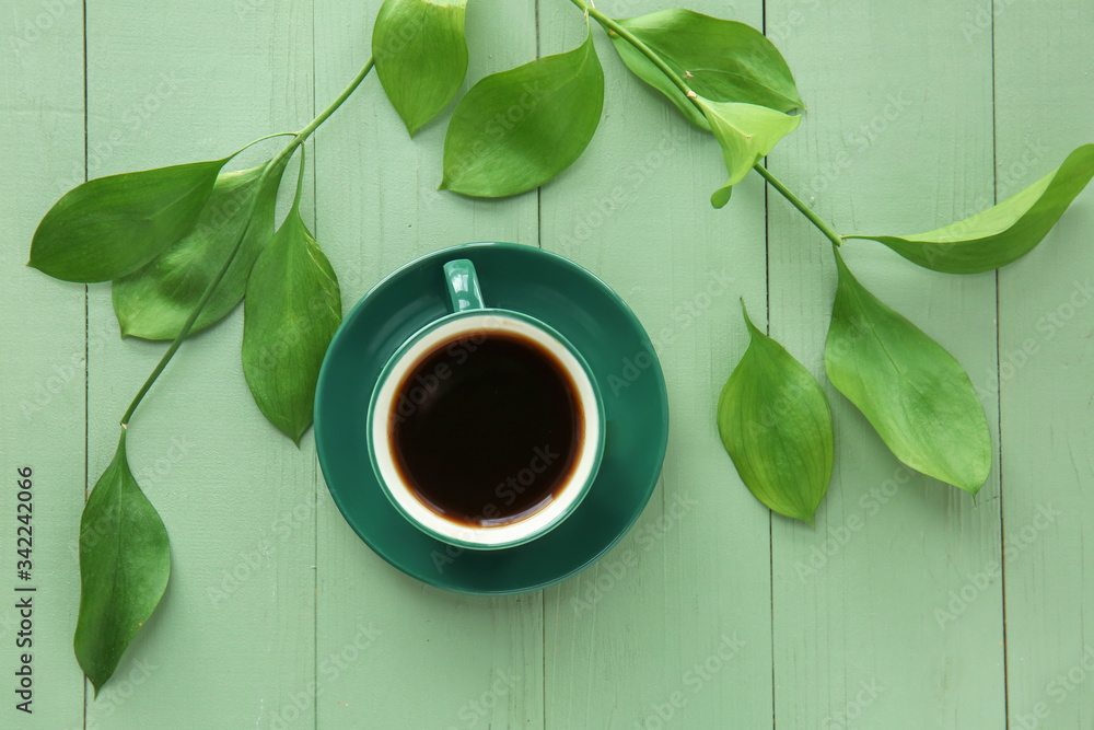 Cup of coffee and green leaves on color wooden background