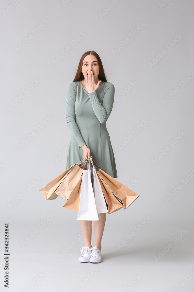 Surprised young woman with shopping bags on grey background