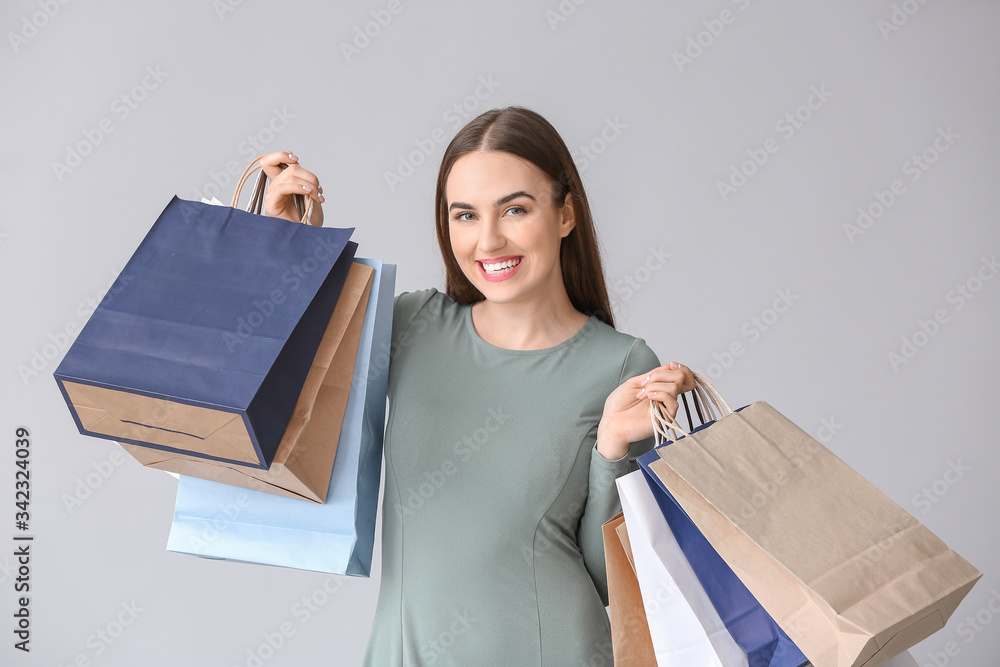 Young woman with shopping bags on grey background