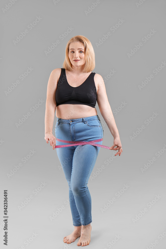 Overweight woman with measuring tape on grey background. Weight loss concept