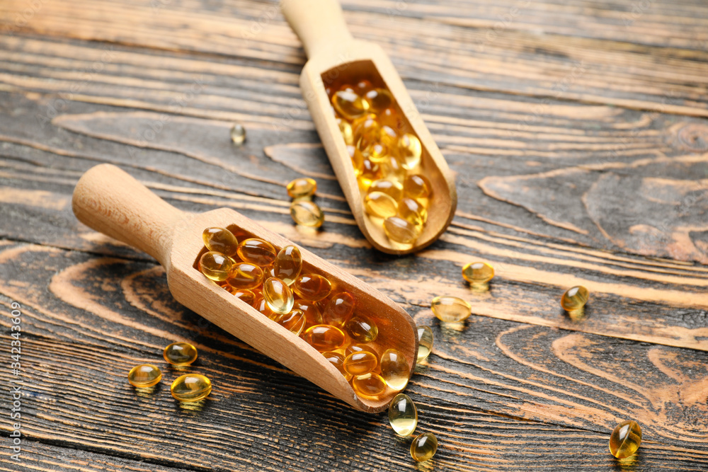 Scoops with fish oil capsules on wooden background