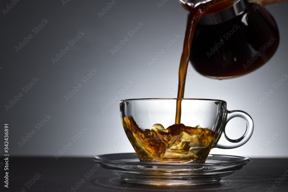 Pouring coffee on a transparent cup on black background