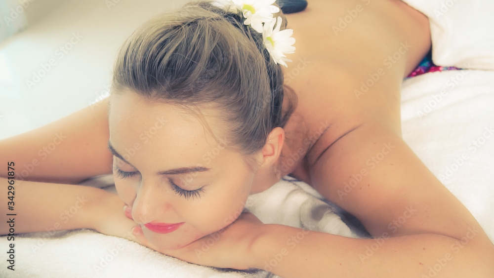 Woman getting hot stone massage treatment by professional beautician therapist in spa salon. Luxury 