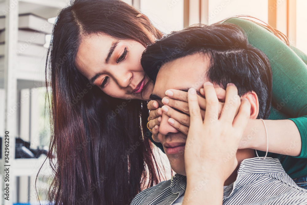 Happy Asian couple play covering eyes in living room.