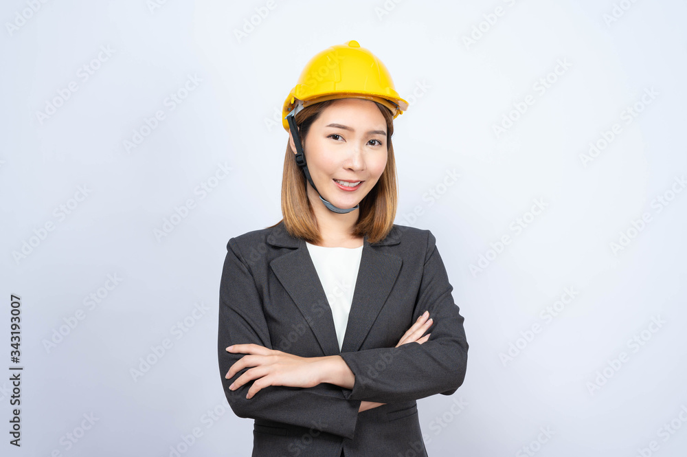 Portrait of Young Asian businesswoman wearing yellow safety-helmet in formal suit smiling looking at