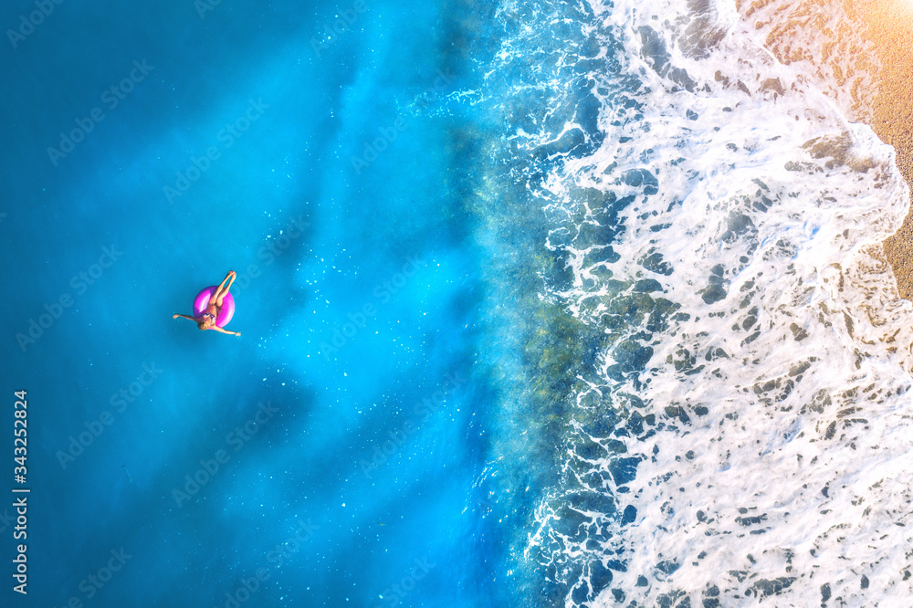 Aerial view of a young woman swimming with the donut swim ring in the clear blue sea with waves at s