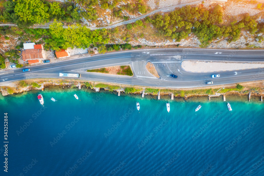 Aerial view of road in beautiful green forest and boats in the sea at sunset in summer. Colorful lan