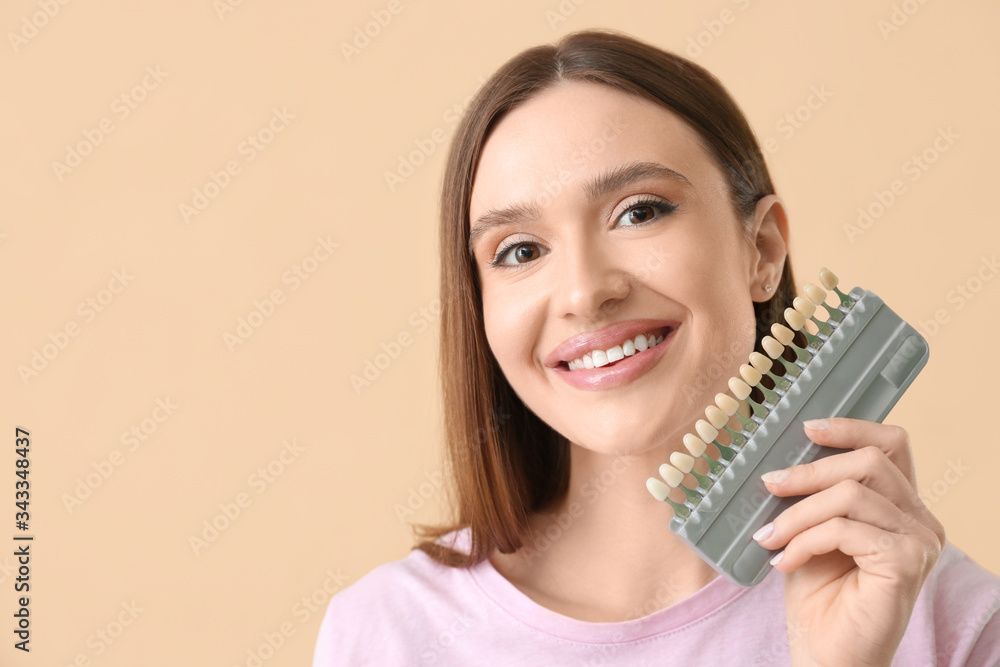 Beautiful young woman with teeth color samples on beige background