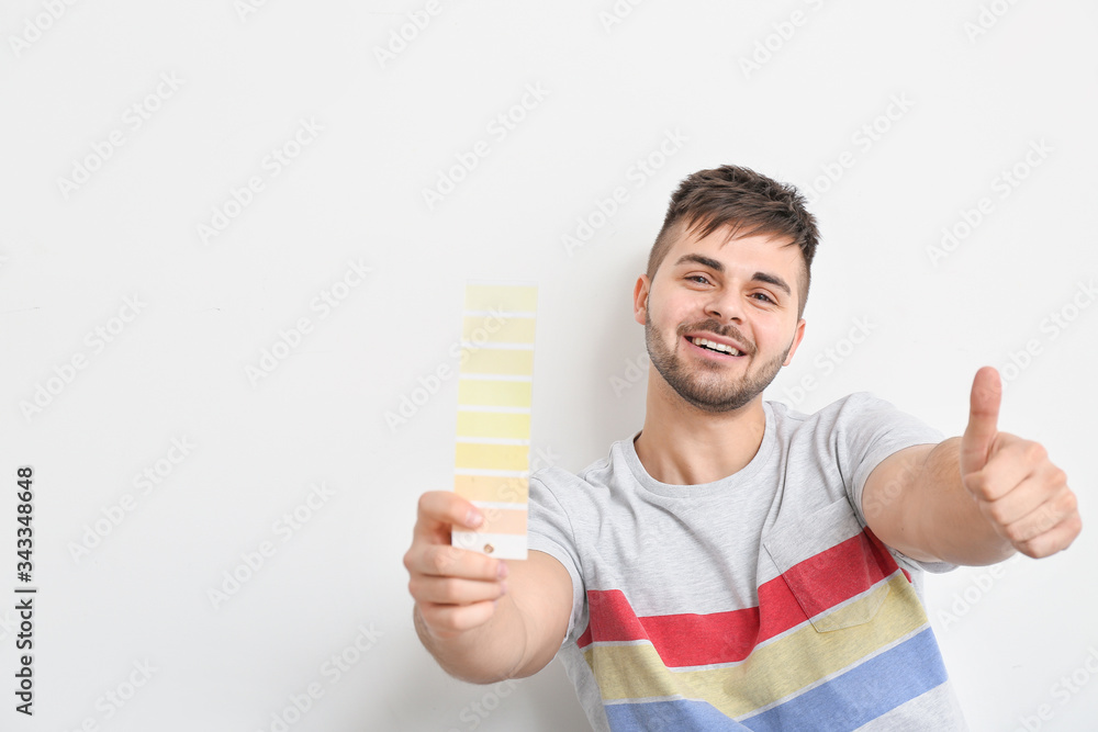 Young man with color swatches showing thumb-up gesture on white background