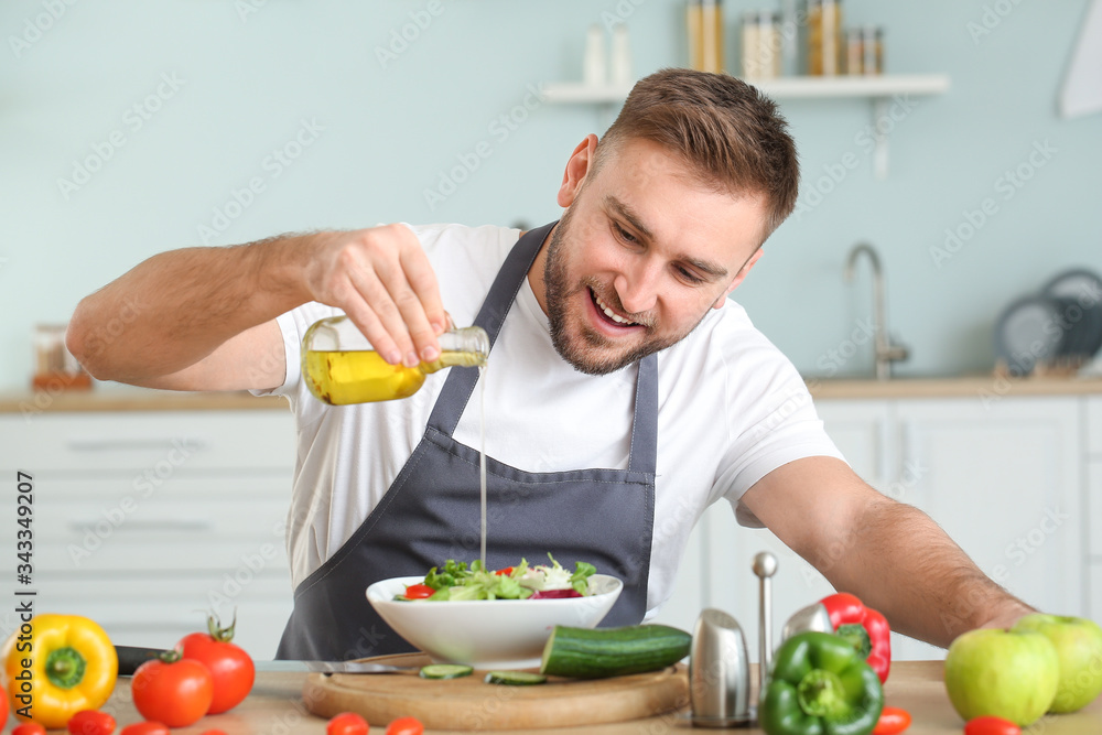 Handsome male chef dressing salad in kitchen