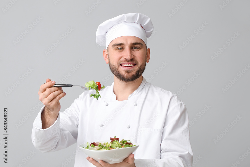 Handsome male chef with salad on light background