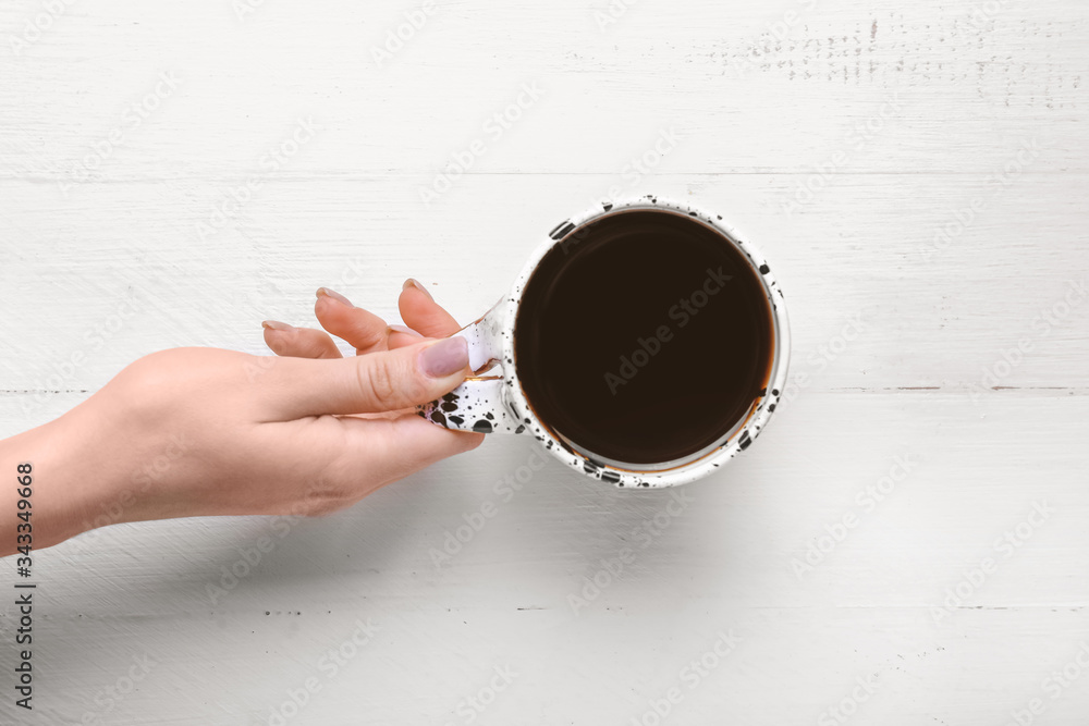 Female hand with cup of coffee on white wooden background