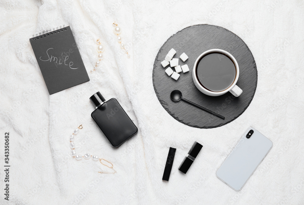 Composition with cup of coffee, mobile phone, perfume, notebook and cosmetics on white plaid