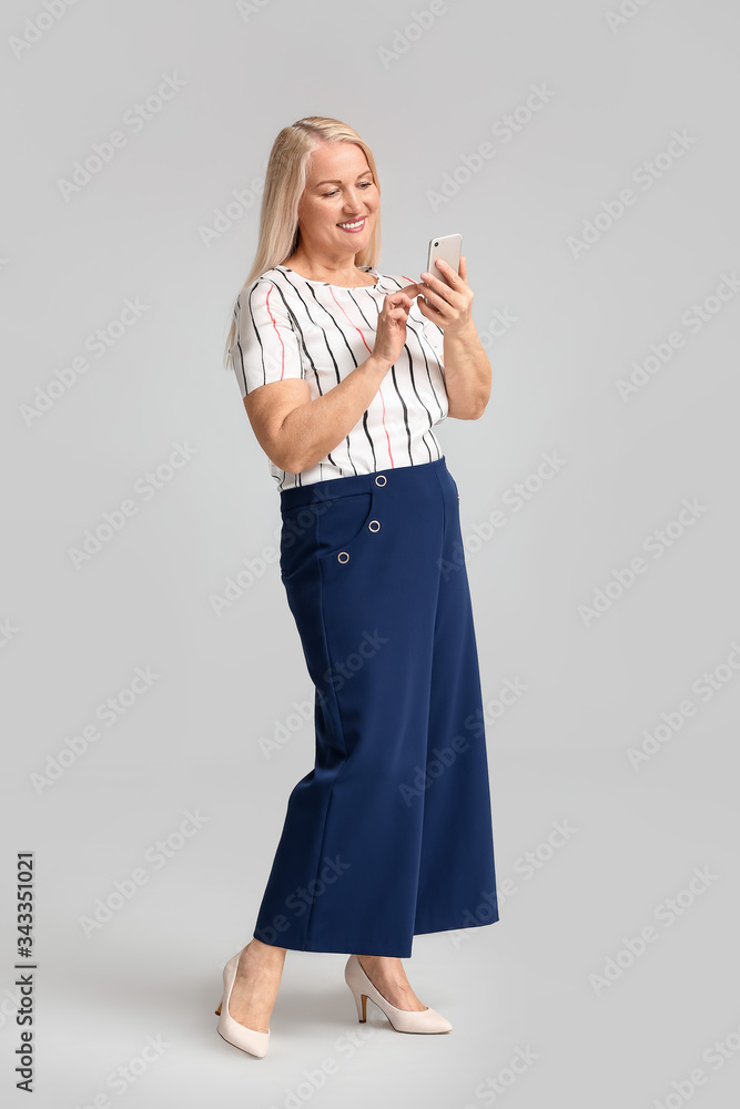 Portrait of mature businesswoman with mobile phone on light background