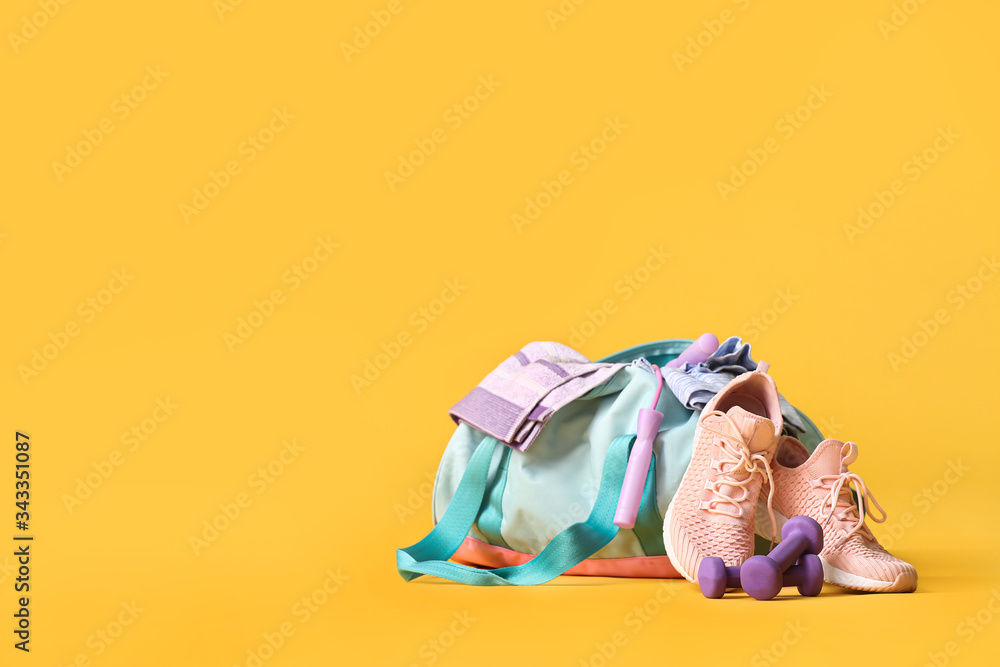 Bag with sportswear and equipment on color background