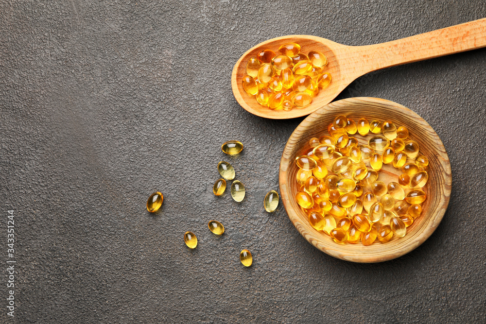 Bowl and spoon with fish oil capsules on grey background