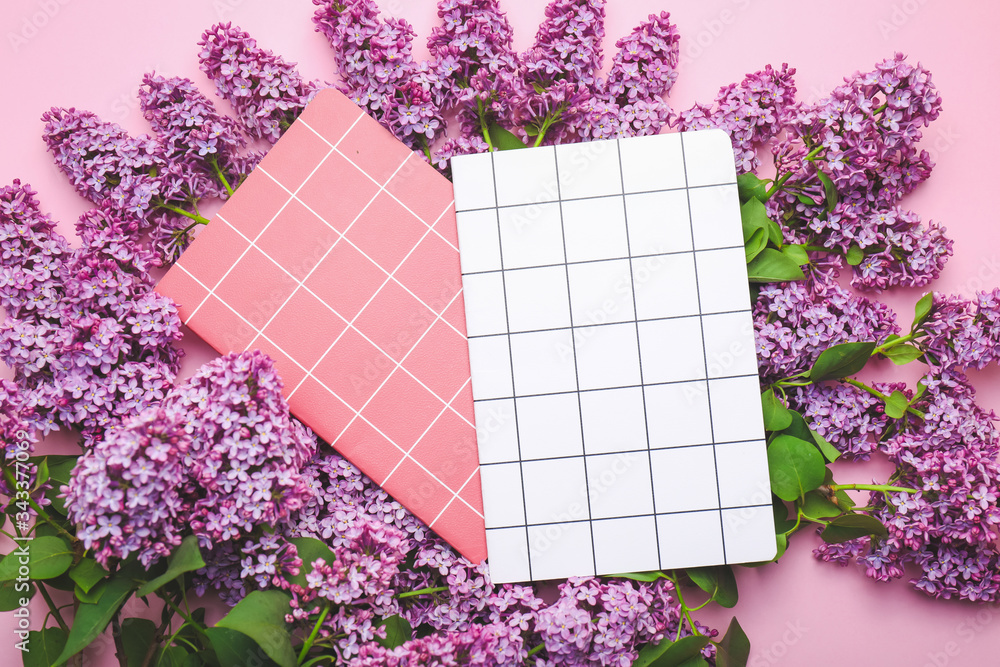 Beautiful lilac flowers and notebooks on color background